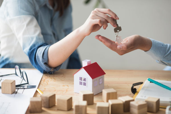 Close-up picture of a woman's hand delivering some keys to a man and a model house in background - Using a Home Equity Loan for an Airbnb - DG Pinnacle Commercial - Miami Mortgage Lender