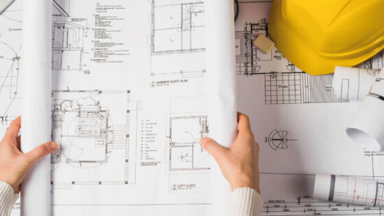 Engineer opening floorplans and bluprints with yellow helmet | Best 2022 Markets for Ground Up Construction Loans | DG Pinnacle Commercial - Miami Mortgage Lender