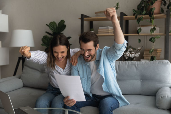 Happy young couple having some good news sitting on their couch | Who is eligible for Non-QM Loans | DG Pinnacle Commercial - Miami Mortgage Lender