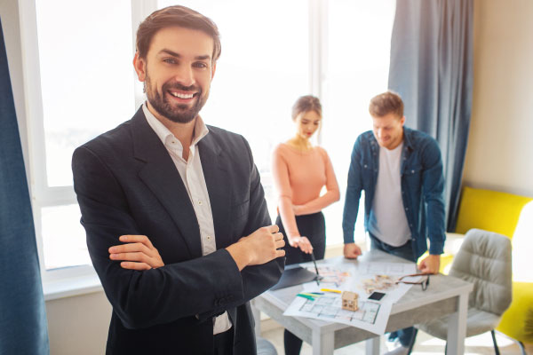 Smiling male mortgage officer at office with a couple in background - 5 Mortgage Lending Strategies to Help Your Customers | DG Pinnacle Commercial | Miami Wholesale Mortgage Funding Lender